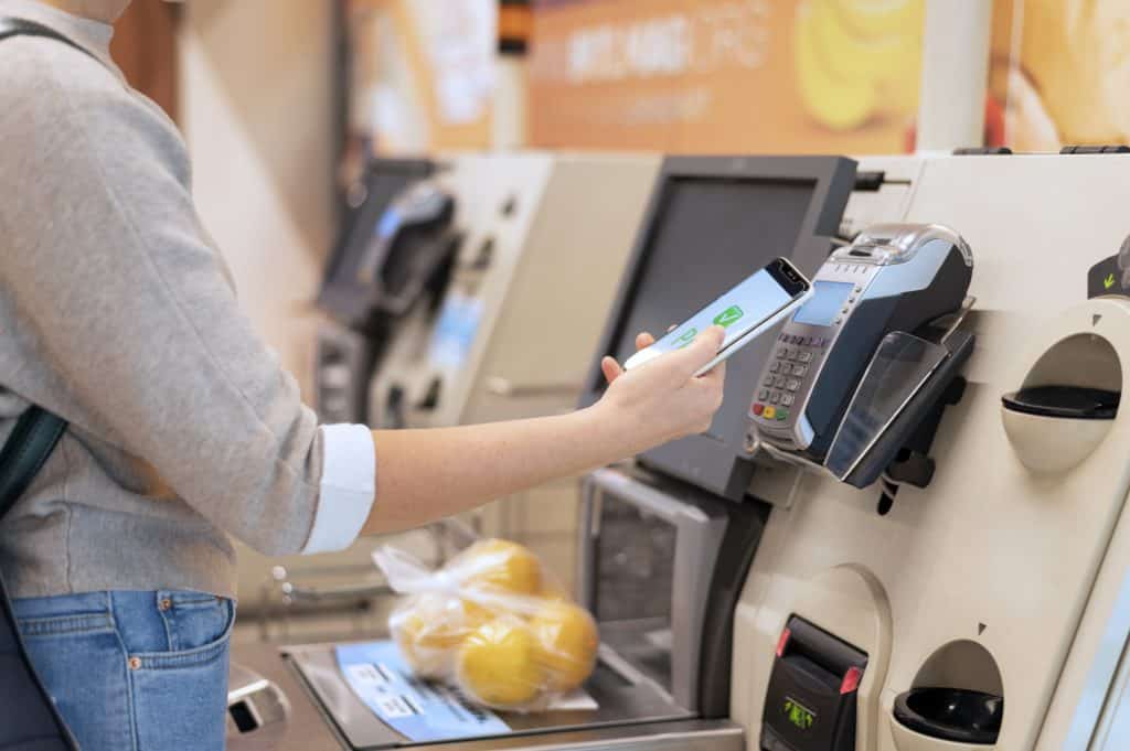 Person paying with her smartphone using e-wallet at a self-checkout kiosk.