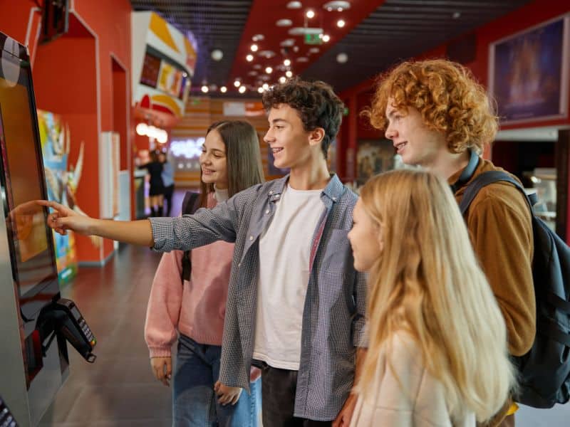 Group of friends placing orders at self-service kiosks in a mall food court.