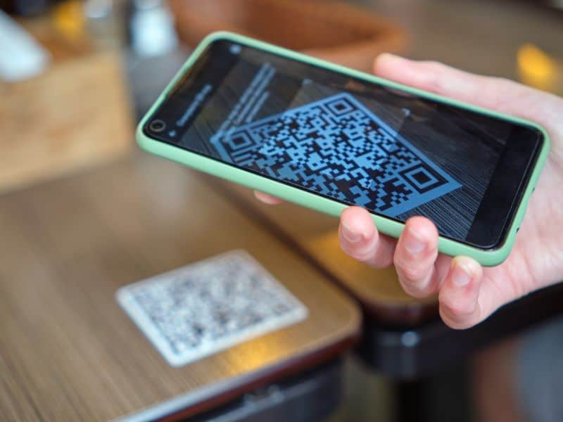 QR Ordering. A close-up image of a hand holding a phone to scan a QR code on a table.